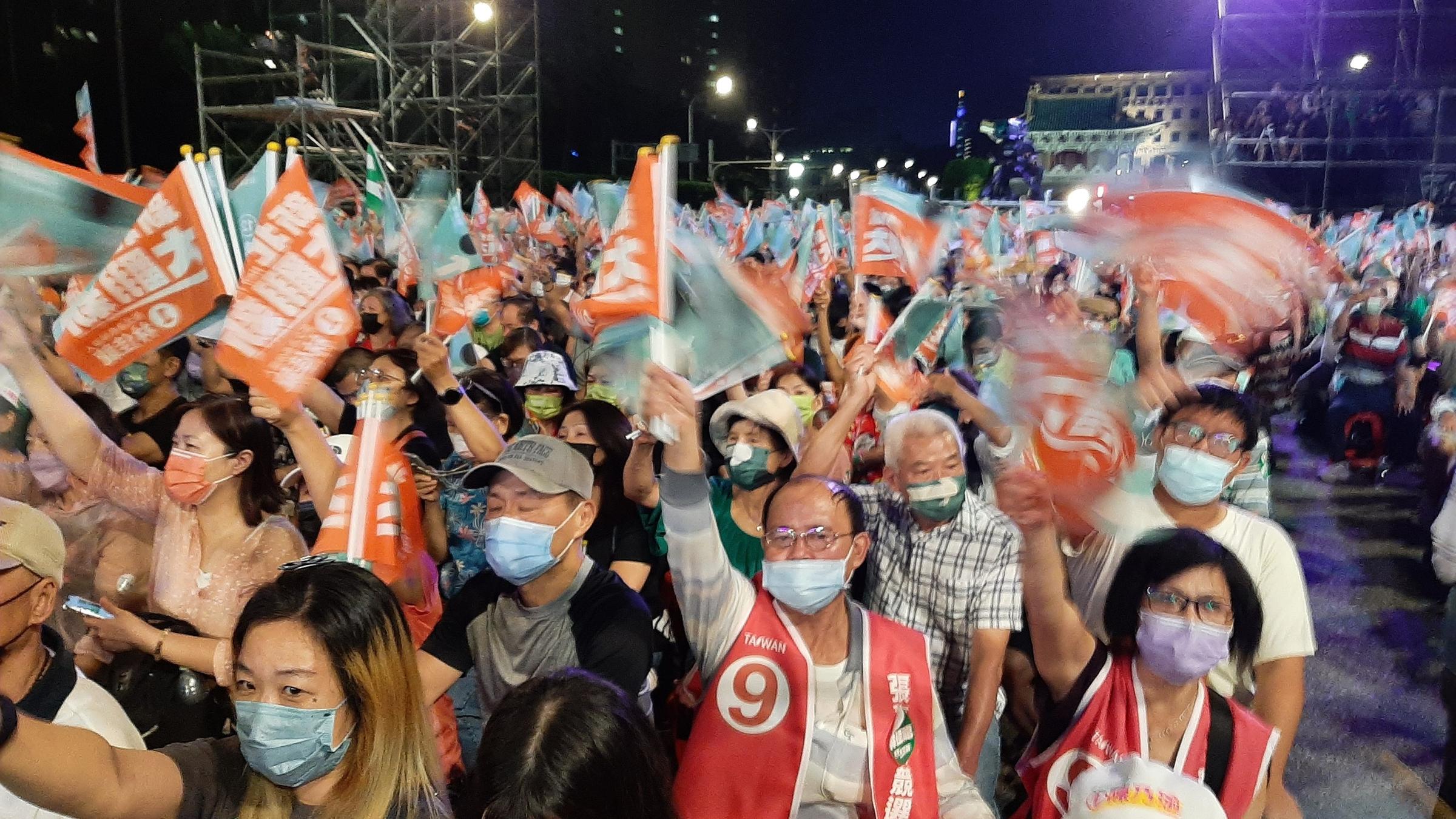"Taiwan – Angst vor der Invasion": Menschenmenge mit orangenen Flaggen bei einer Wahlkampfveranstaltung.