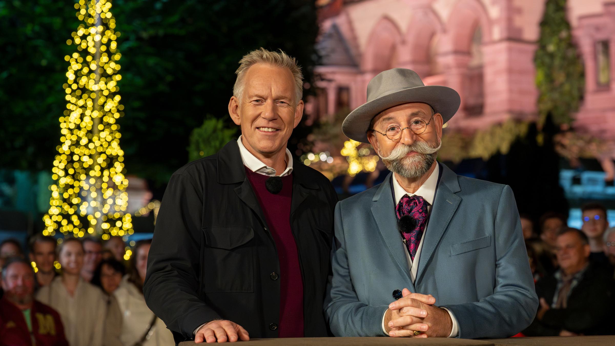 "Bares für Rares - Deutschlands größte Trödelshow": Johannes B. Kerner und Horst Lichter stehen dicht nebeneinander hinter dem Expertisentisch. Sie lächeln in die Kamera. Hinter ihnen steht Publikum vor dem weihnachtlich geschmückten Park von Schloss Drachenburg.
