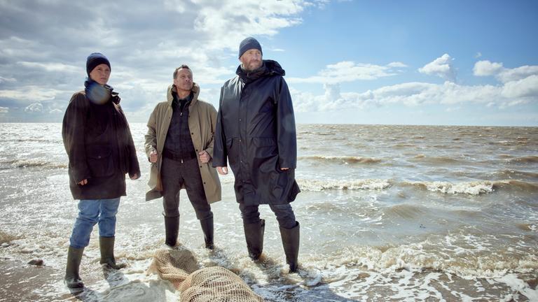 "Ostfriesenwut": Ann Kathrin Klaasen (Picco von Groote) steht im seichten Wasser neben ihren Kollegen Rupert (Barnaby Metschurat) und Frank Weller (Christian Erdmann) vor einer angespülten Leiche. Die Leiche ist in ein Fischernetz gewickelt.