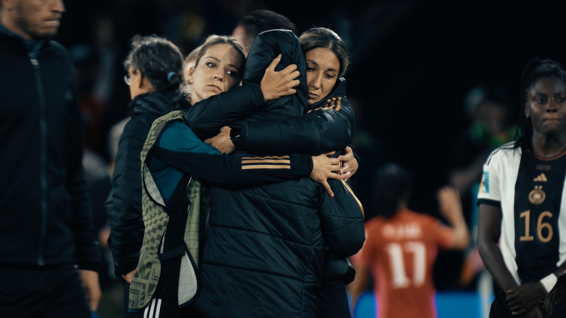 "Born for this – Mehr als Fußball": Nach dem Vorrunden-Aus bei der WM 2023 liegen sich drei Frauen mit enttäuschten Gesichtern in den Armen.