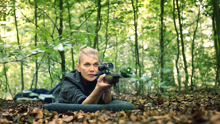 "Helen Dorn - Das Recht zu schweigen": Helen Dorn (Anna Loos) liegt bäuchlings mit einem Gewehr im Anschlag auf dem Waldboden.