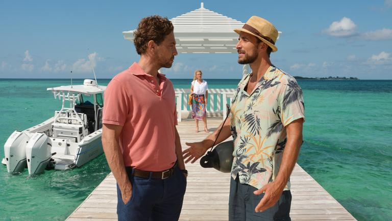 "Das Traumschiff - Bahamas": Auf einem Anlegesteg stehen sich Toby Heers (Max Alberti) und Philip Singer (Leander Lichti) gegenüber und reden miteinander. Im Hintergrund steht Melanie Singer (Aline Hochscheid) und beobachtet die beiden.