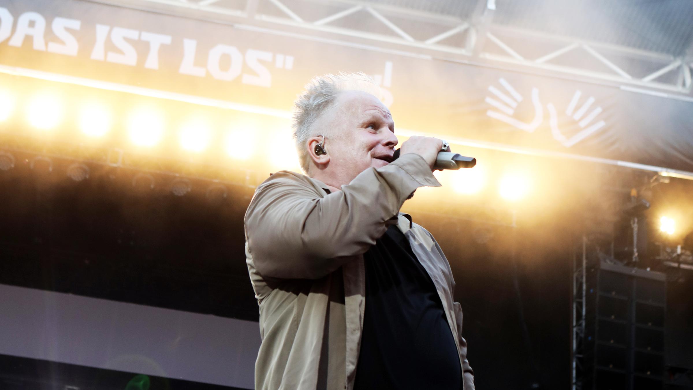 "Herbert Grönemeyer: Das ist los Tour 2023": Herbert Grönemeyer steht auf der Bühne. Er hält ein Mikro in der Hand und singt, im Hintergrund sind Scheinwerfer zu erkennen.