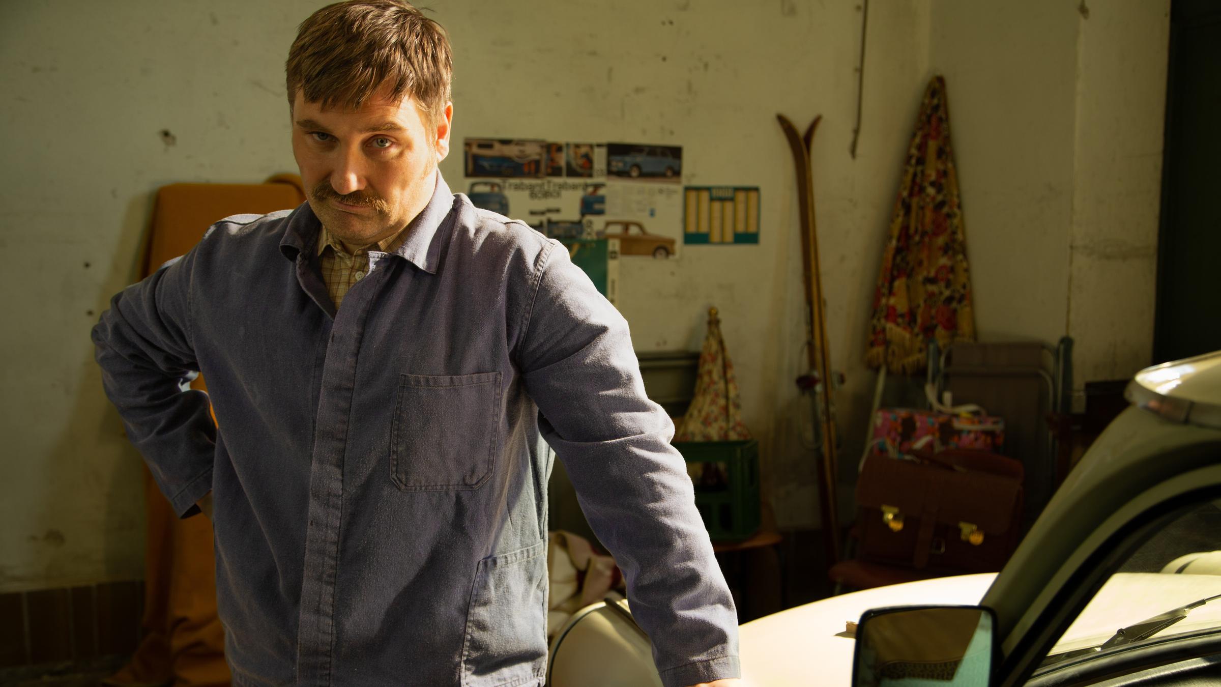 "Terra X History: Ein Tag in der DDR - Der Trabi-Krimi": Thomas B. (Sebastian Thiers) im Blaumann, an einen Trabant gelehnt.