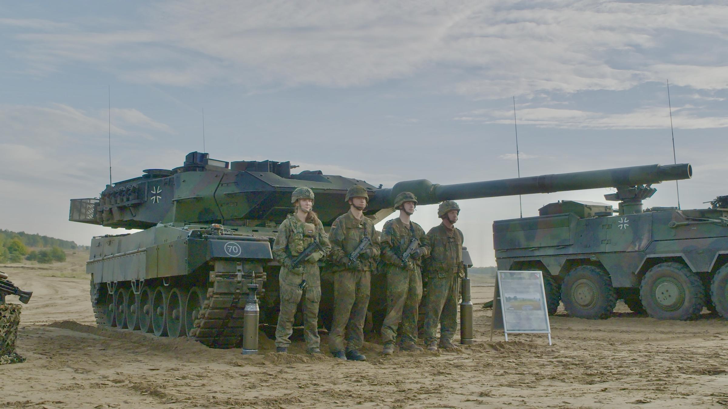  "Rüstungsboom - Bomben, Panzer und Probleme": Vier Soldaten der Bundeswehr stehen in Tarnuniform vor einem Leopard 2 Panzer. Daneben steht ein weiterer Panzer.