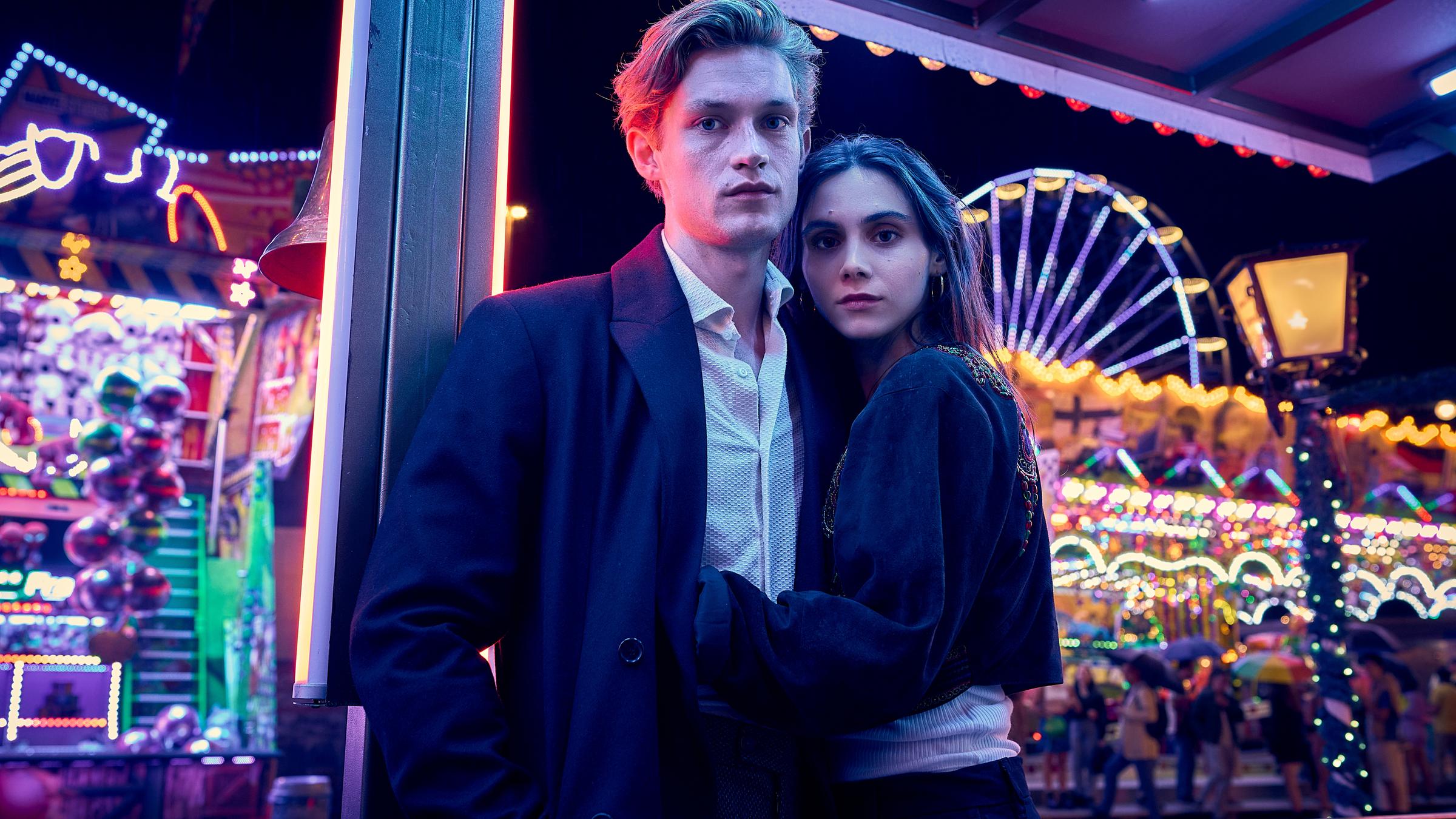 "Love Sucks" Drehstart. Ben (Damian Hardung) Zelda (Havana Braun) umarmen sich. Im Hintergrund ist eein Rummelplatz in bunter, nächtlicher Beleuchtung zu sehen.