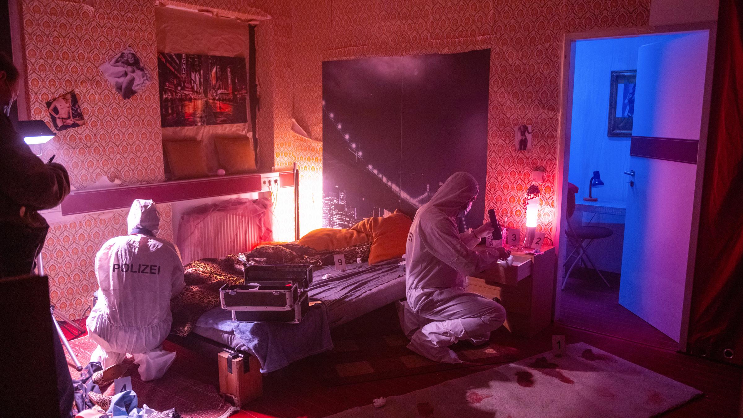 "Aktenzeichen XY... Cold Cases": Nachgestellte Szene in einem Schlafzimmer im Laufhaus. Zwei Polizisten der Spurensicherung durchsuchen das verwüstete Zimmer.