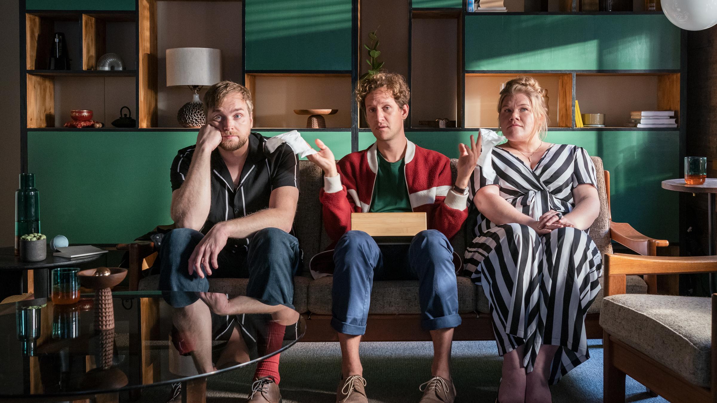 "Familie Anders - Willkommen im Nest": Fabian Anders (Moritz Treuenfels) sitzt auf einer Couch zwischen Tom (Knud Riepen) und Tess Scharper (Gisa Flake). Er hält eine Packung Taschentücher auf dem Schoß und streckt beiden jeweils ein Taschentuch hin.