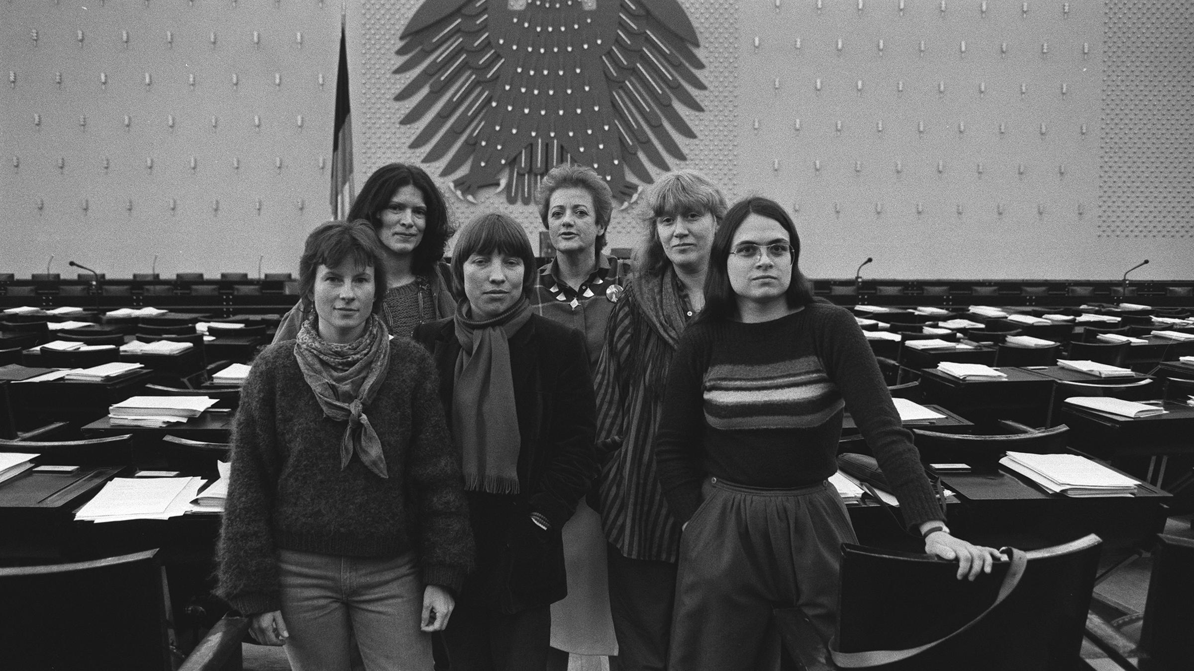 "Die Unbeugsamen": SW-Fotos von 1984: eine Gruppe von sechs Frauen steht zusammen, im Hintergrund die leeren Abgeordnetentische und Regierungsband des deutschen Bundestages in Bonn. Es sind die Sprecherinnen der Fraktion der Partei Die Grünen.