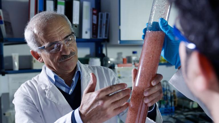 "planet e.: Fracking in Deutschland – Rettung aus der Energiekrise oder Risiko?": Prof. Amro hält im Labor einen Glaszylinder mit einer rötlichen Flüssigkeit in der Hand.