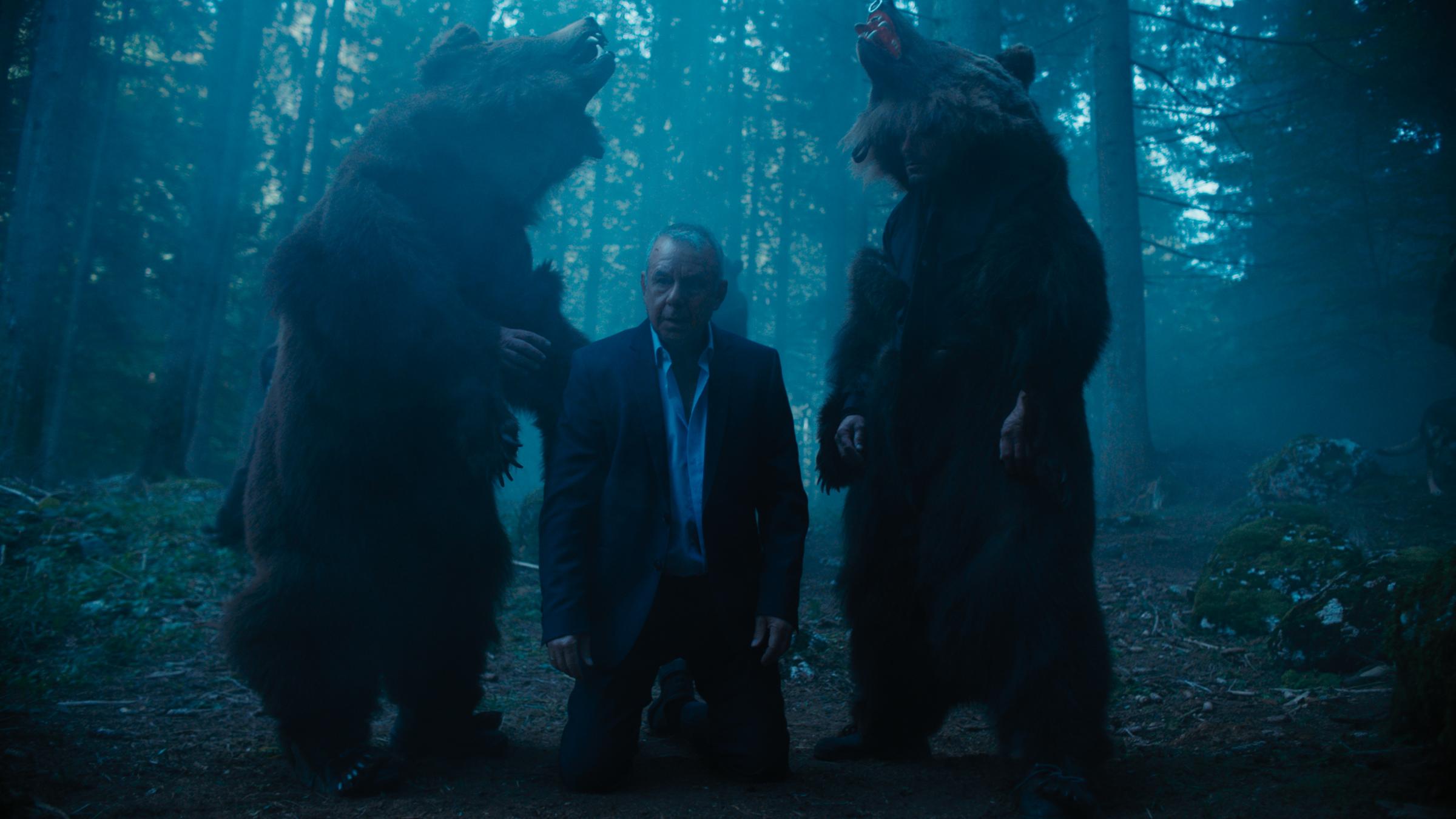 "Blutholz": Es ist Nacht in den rumänischen Wäldern. Hans Schüssler (Joachim Król) kniet zwischen zwei Menschen in Bärenkostümen.