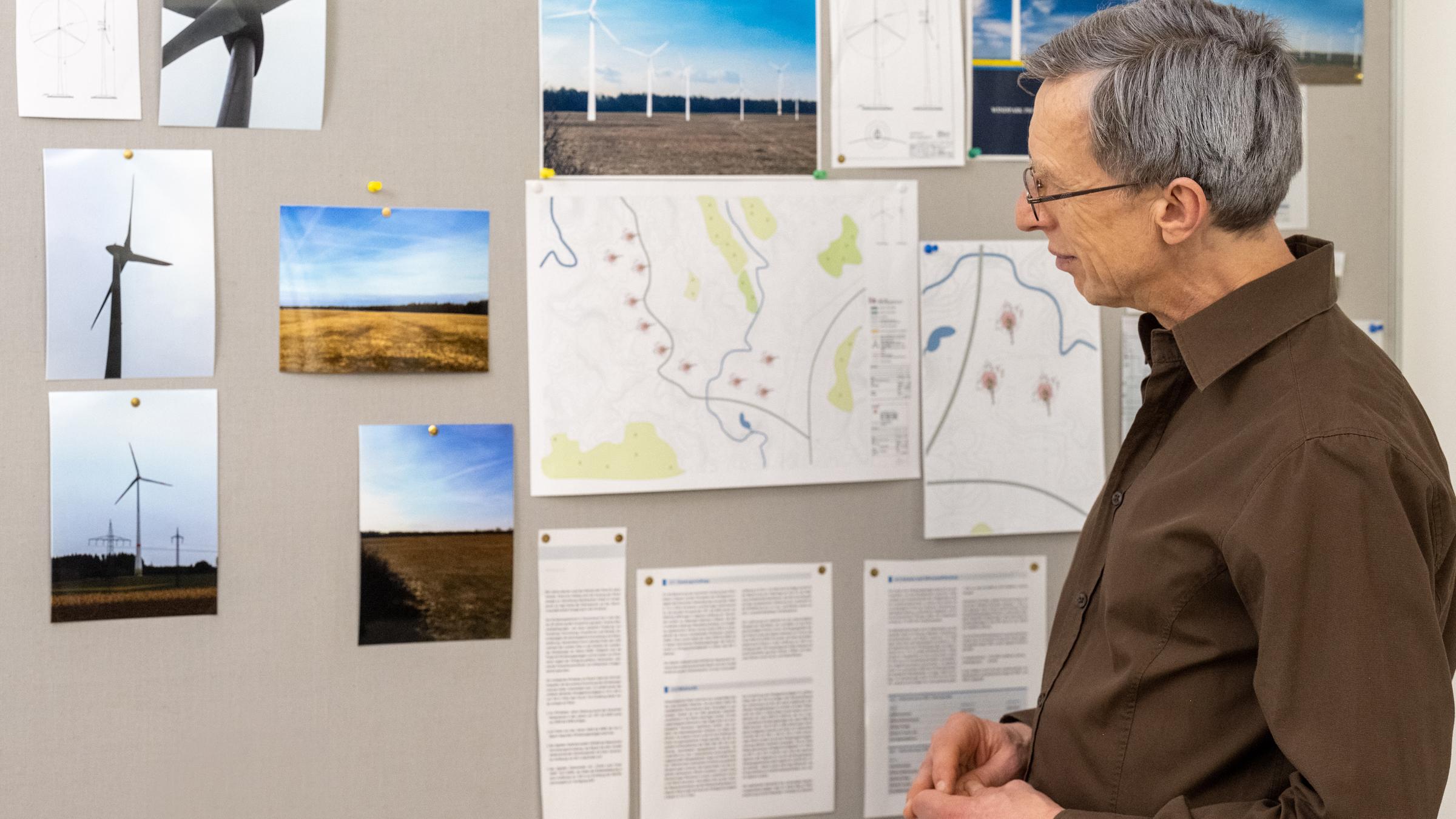 "Aktenzeichen XY... Vorsicht, Betrug!": Nachgestellte Szene. Ein älterer Mann mit Brille und braunem Hemd steht vor einer Infotafel über Windräder und betrachtet die unterschiedlichen Inhalte.