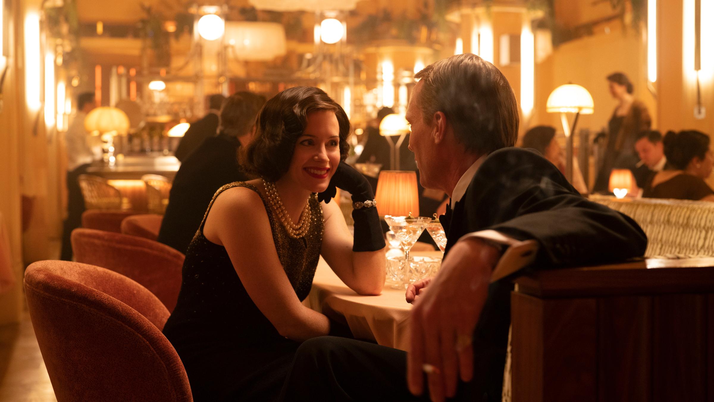 "A Very British Scandal: Herzogin von Argyll": Margaret (Claire Foy) und Ian (Paul Bettany) sitzen in einem Club am Tisch und flirten miteinander.