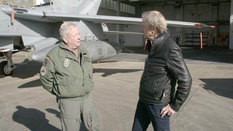 "ZDFzeit: Putins Tabubruch - die neue Angst vor der Bombe": Oberst Thomas Schneider und Claus Kleber stehen vor einem Kampfflugzeug und unterhalten sich.