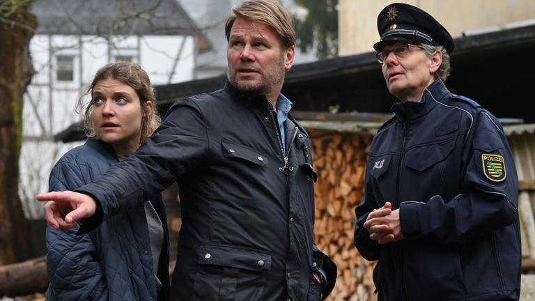 "Erzgebirgskrimi - Familienband": Die Kommissare Robert Winkler (Kai Scheve) und Karina Szabo (Lara Mandoki) schauen zusammen mit Polizeihauptmeister Wagner (Thomas Bading) nach links in die Ferne. Robert Winkler zeigt mit dem Finger in die Richtung in die sie schauen.