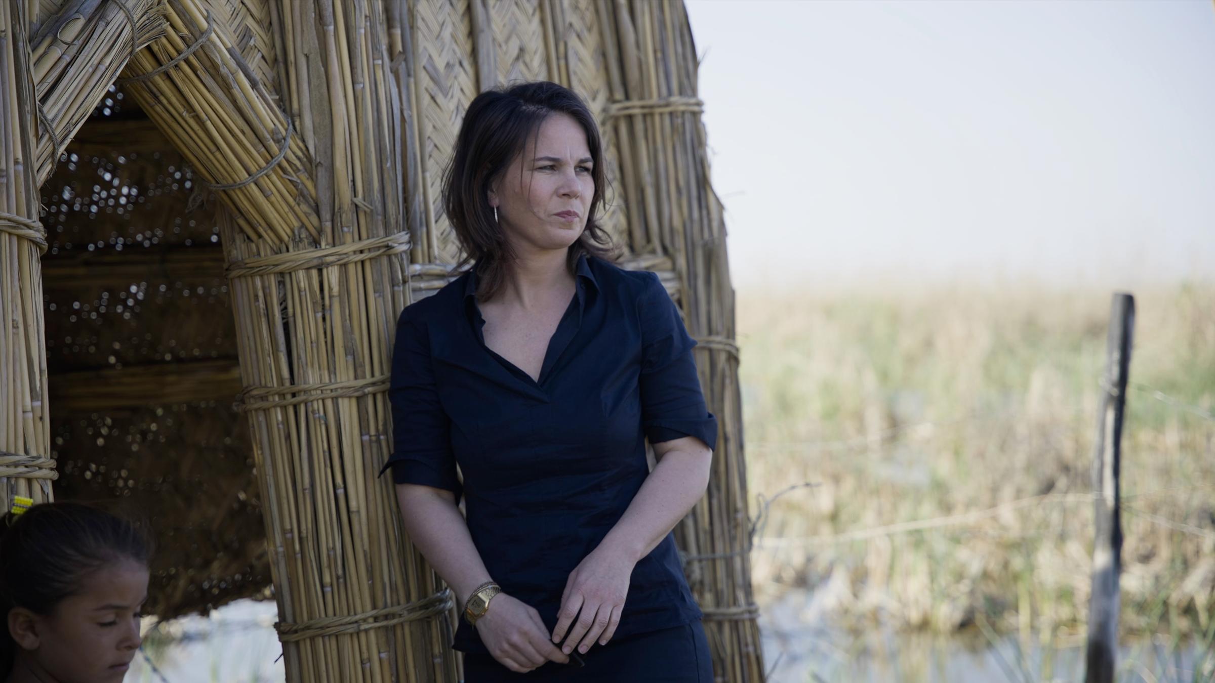 "ZDFzeit: Mensch Baerbock! Die undiplomatische Diplomatin":  Vor einer Hütte aus Bambus steht Ministerin Baerbock, mit beobachtendem Blick.