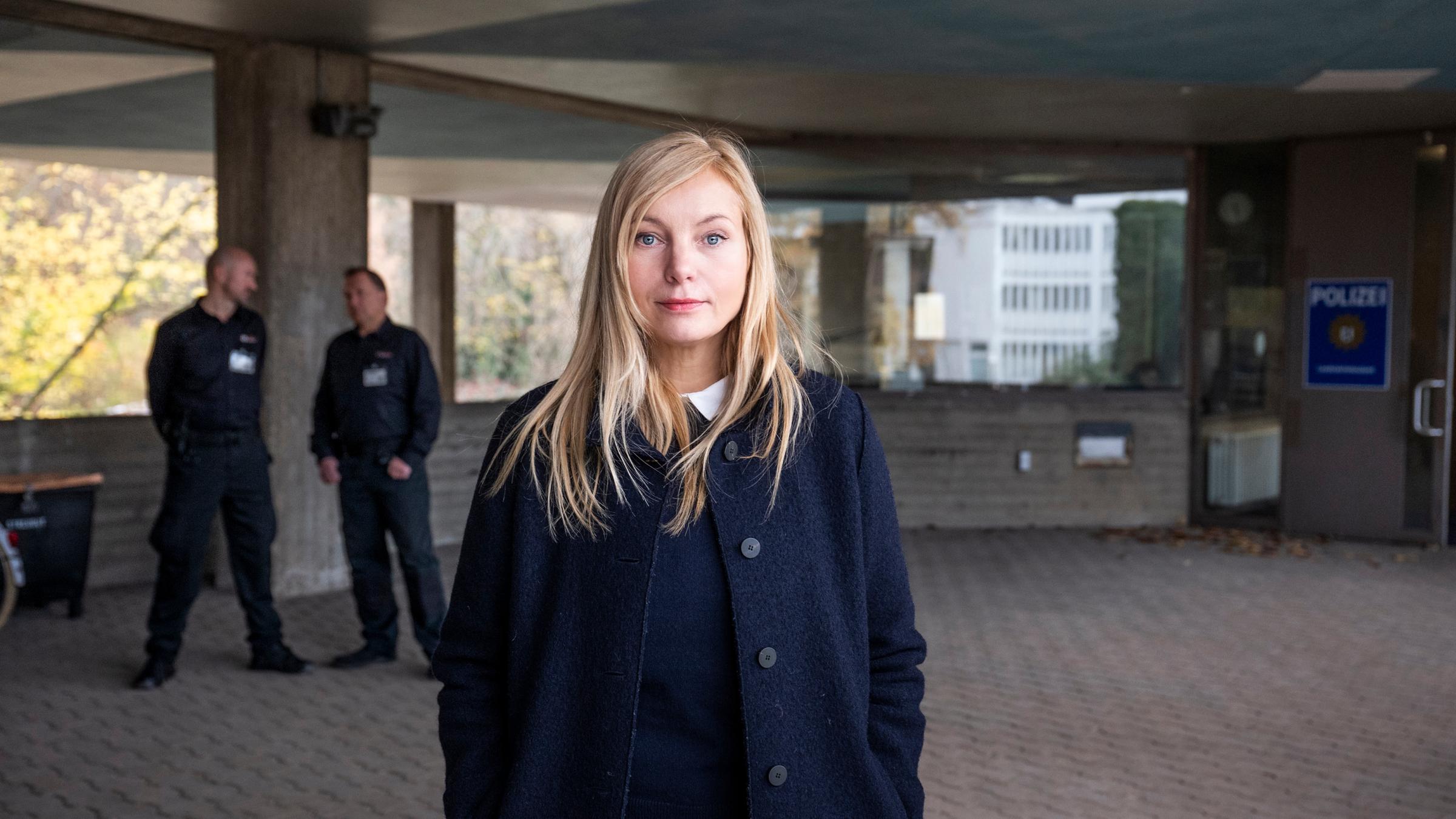"Die Jägerin - Riskante Sicherheit": Staatsanwältin Judith Schrader (Nadja Uhl) steht vor dem LKA Berlin. Hinter ihr stehen zwei Männer eines externen Wachschutzes (Komparsen).