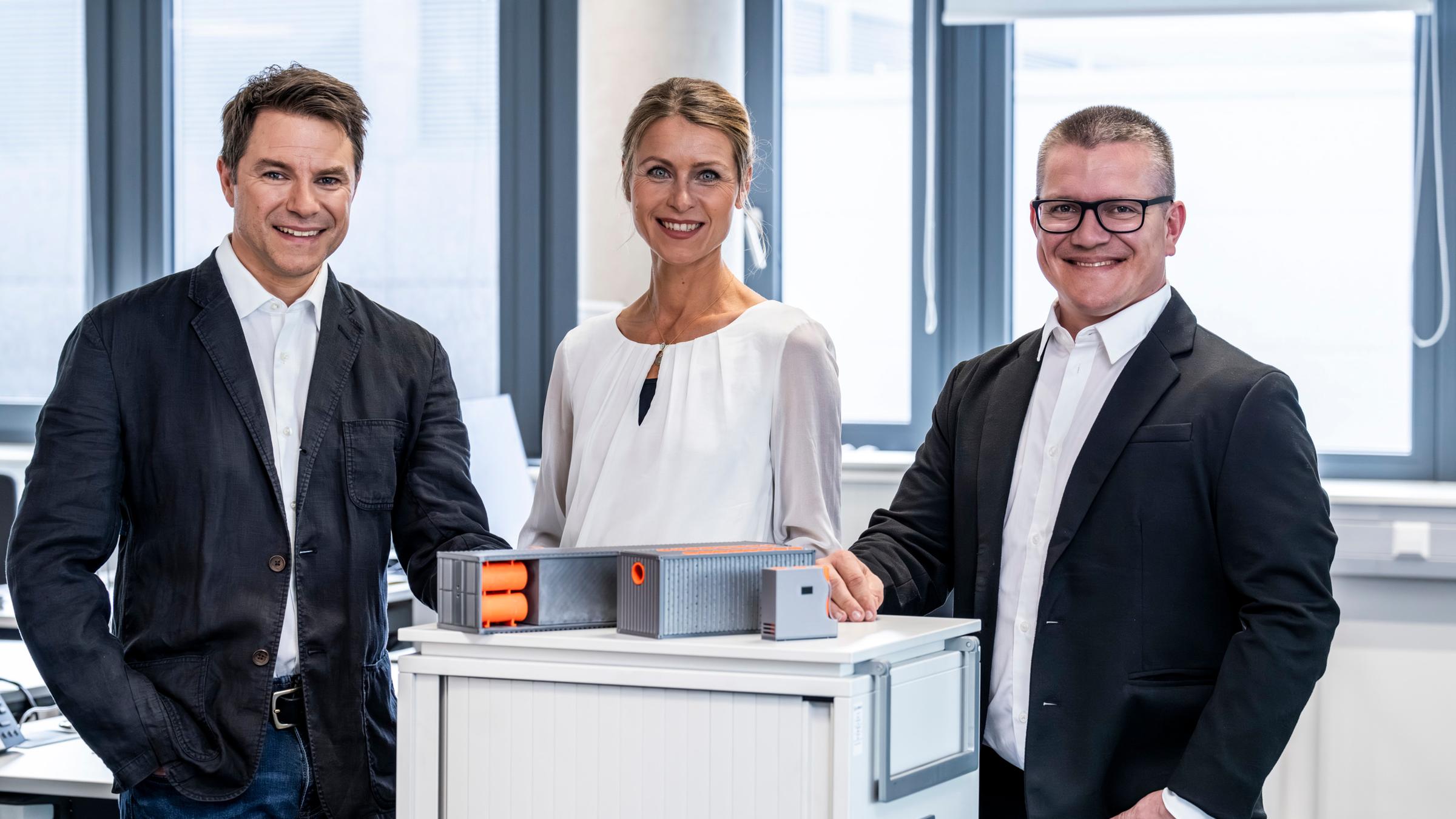 "Deutscher Zukunftspreis 2023 - Preis des Bundespräsidenten für Technik und Innovation": Zwei Männer und eine Frau aus Team 2 stehen nebeneinander in einem Raum und lächeln in die Kamera.