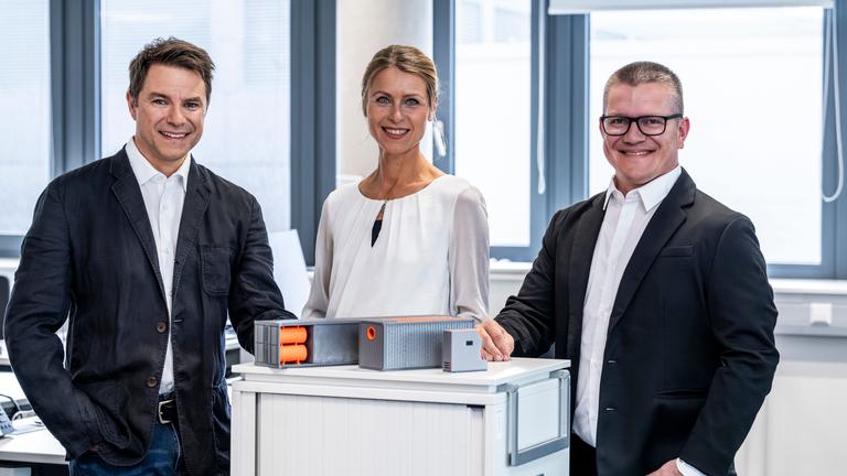 "Deutscher Zukunftspreis 2023 - Preis des Bundespräsidenten für Technik und Innovation": Zwei Männer und eine Frau aus Team 2 stehen nebeneinander in einem Raum und lächeln in die Kamera.