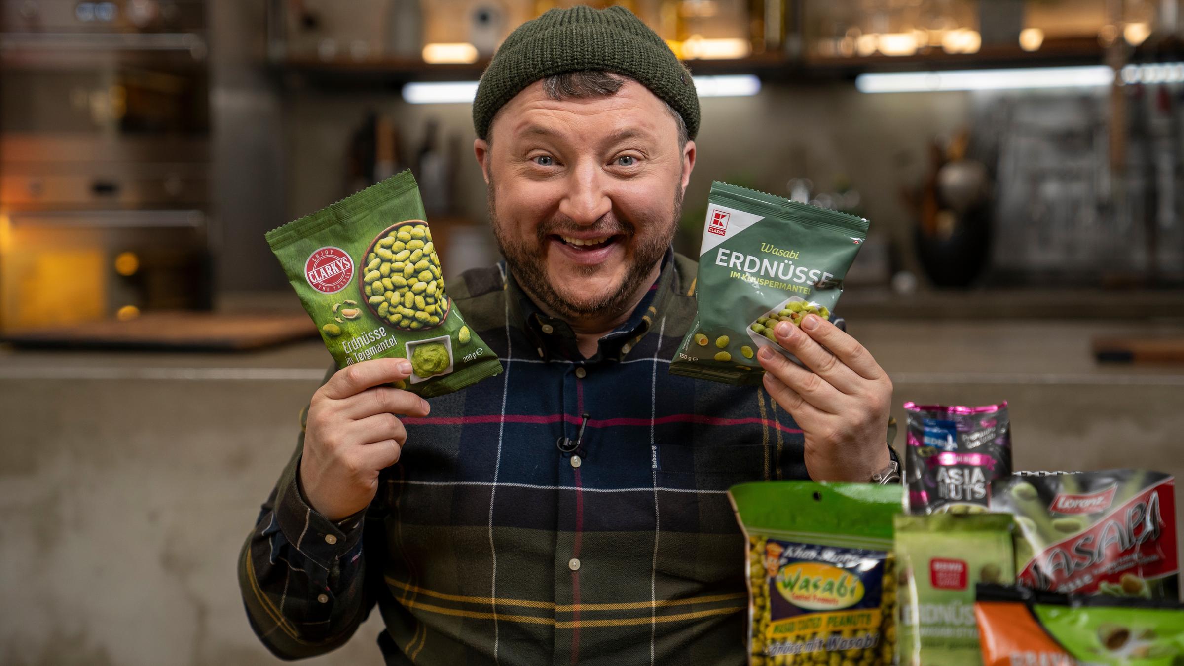 "Lebensmitteltricks - Lege packt aus - Miese Maschen im Snack-Regal": Sebastian Lege hält lachend zwei Wasabi-Nuss-Packungen hoch.