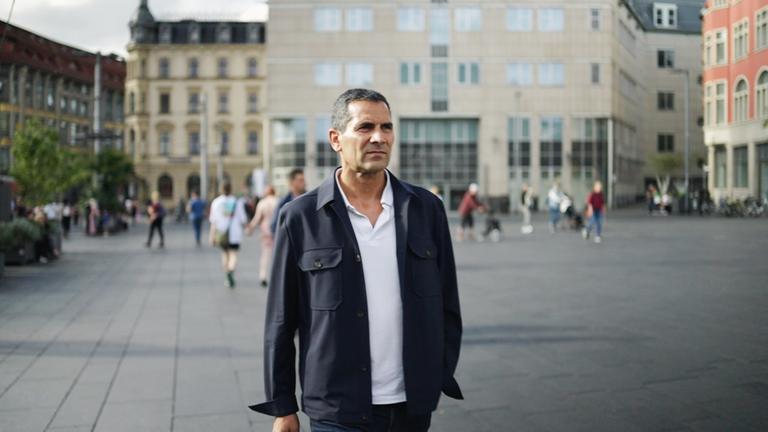 "Am Puls mit Mitri Sirin": Mitri Sirin überquert einen Platz und schaut in die Ferne.
