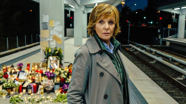"Kommissarin Lucas - Helden wie wir": Kommissarin Lucas (Ulrike Kriener) steht bei Nacht an einem leeren Bahnsteig. Im Hintergrund befinden sich Grablichter, Blumen und handgeschriebene Briefe.