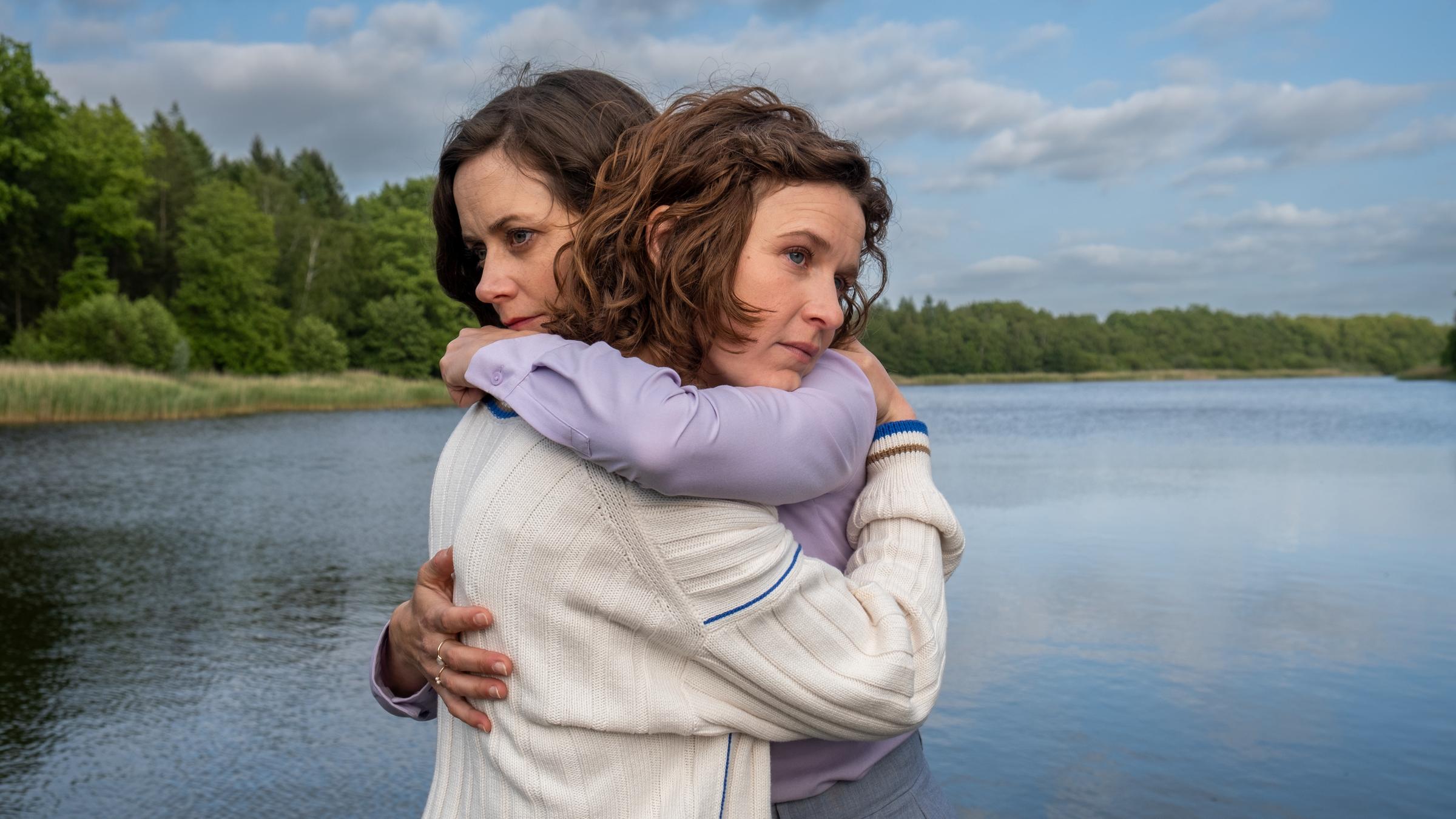 "Malibu – Schwesterherzen": Jantje (Karla Nina Diedrich) und Merle Petersen (Anja Knauer) umarmen sich. Sie stehen auf einem Steg am See. Beide gucken gedankenverloren in die Ferne.