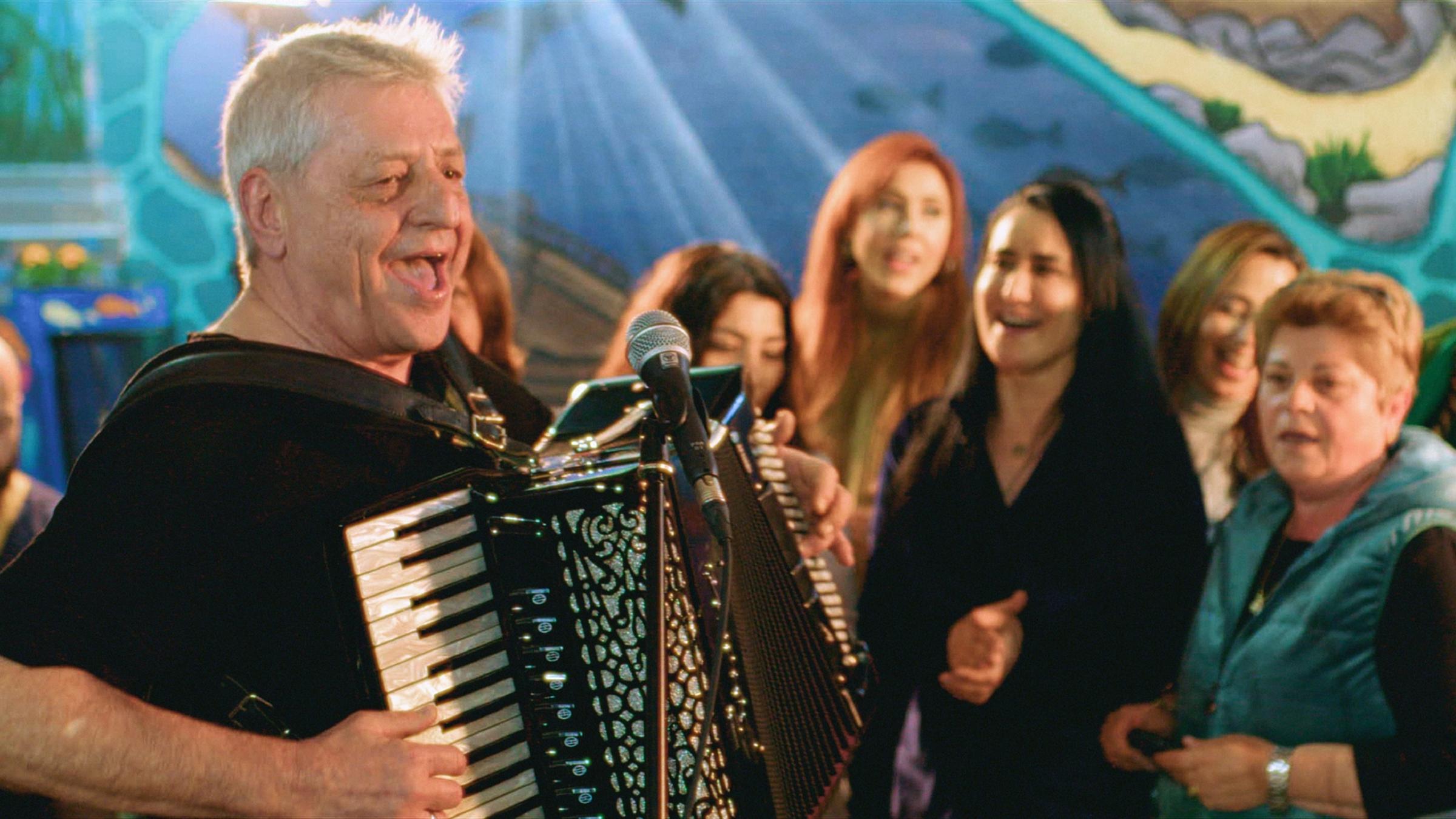 "Deutschlandlieder - Almanya Türküleri": Mann am Akkordeon auf der Bühne vor Frauen.