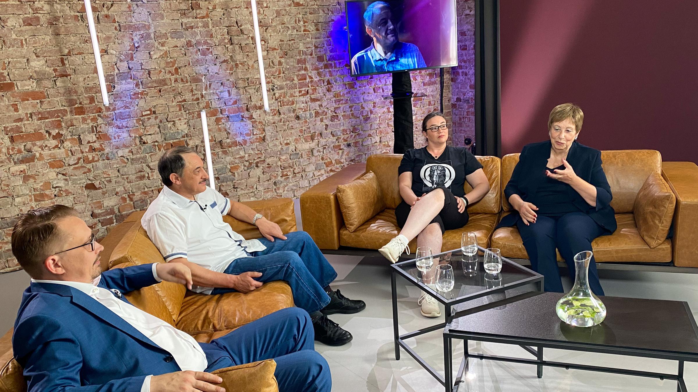 "Die Streitrepublik": Die Protagonisten Kris und Heiko sowie Rebecca und Christina sitzen sich auf zwei Sofas gegenüber, im Hintergrund steht ein Fernseher.