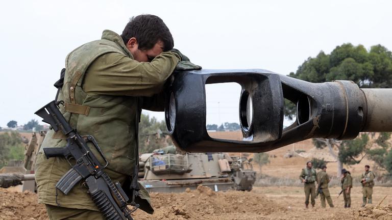 "ZDFzeit: Eskalation in Nahost: Was passiert in Israel?": Soldat mit umgehängtem Gewehr hat seine Hände vor dem Kopf verschränkt und diesen auf das Kanonenrohr eines Panzers gelegt. Panzer und Soldaten im Gelände im Hintergrund.
