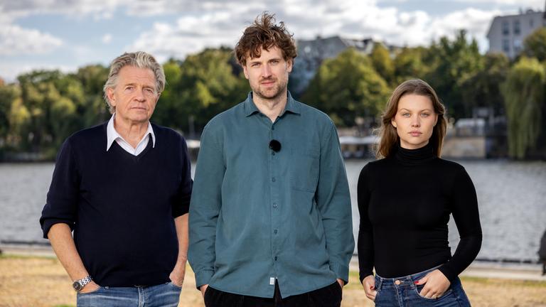 "37°Leben: Risse in unserer Gesellschaft - Jung gegen alt": Daniel Goffart, Ben Bode und Isabelle Vivianne stehen nebeneinander am Flussufer und schauen in die Kamera.