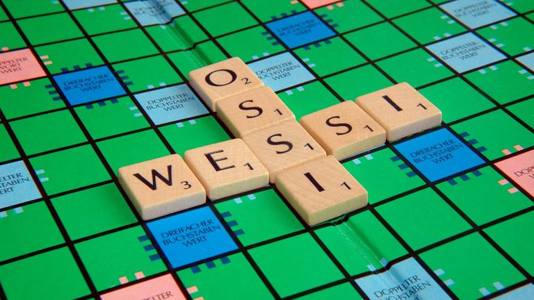 "#WTF - Ostdeutschland in Wessi-Hand": Auf einem Scrabble-Brett überschneiden sich in der Mitte die Worte "Ossi" und "Wessi". Das Wort "Ossi" gibt fünf Punkte und das Wort "Wessi" ergibt sieben Punkte.