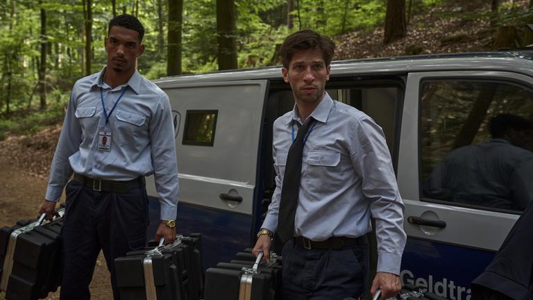  "Der Millionen Raub": Omar Abdallah (Karim Ben Mansur) und Zlatko Petrovic (Slavko Popadić) stehen mit jeweils zwei Koffern in der Hand vor einem Geldtransporter.