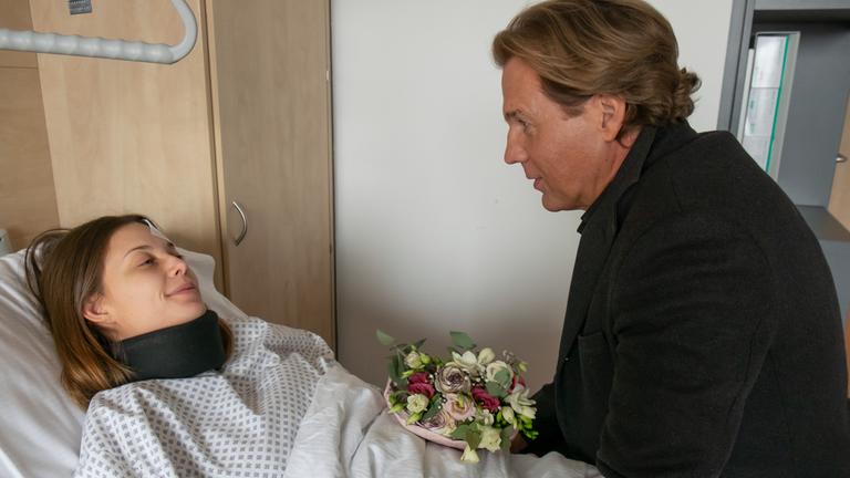 "Der Alte - Crash": Johanna (Lena Meckel) liegt im Krankenhausbett und grinst, als sie ihren Vater sieht, der auf dem Bett sitzt und ihr Blumen vorbeibringt.