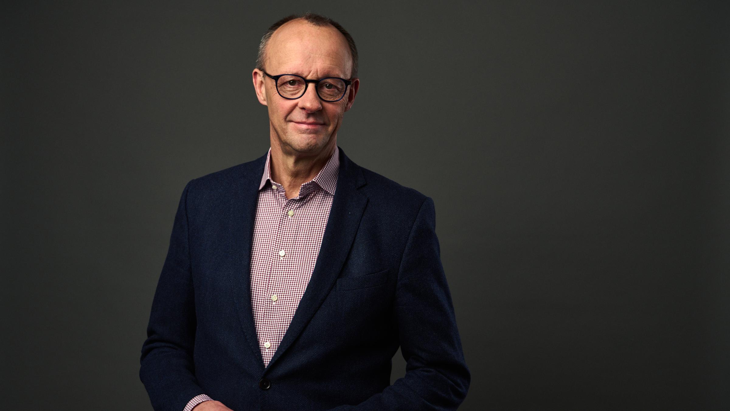 "Mensch Merz! - Der Herausforderer": Großaufnahme des Gesichts von Friedrich Merz vor grauem Hintergrund; er lächelt in die Kamera.