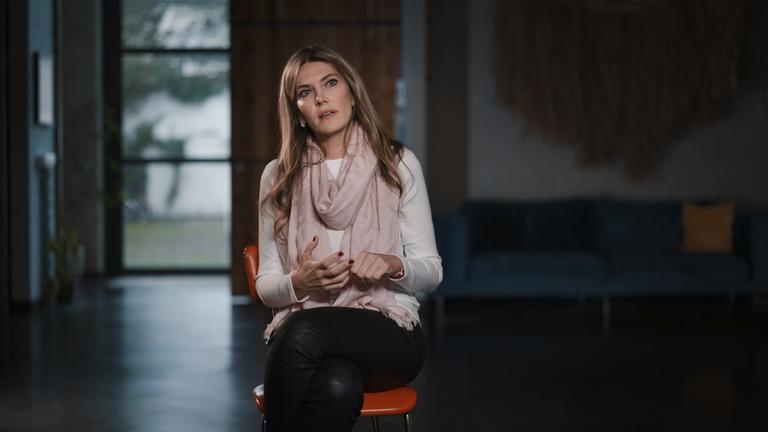 "Gekaufte Politik? - Europa in der Korruptionskrise": Eva Kaili, eine Frau mit langen mittelblonden Haaren sitzt mit dem Blick zur Kamera in einem halbdunklen Raum.