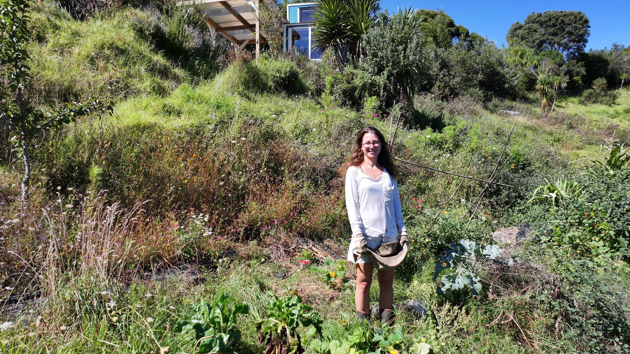 "hallo deutschland - Neuanfang in Neuseeland": Denise Fort steht am Fuß eines Hügels, der mit Gräsern und Büschen bewachsen ist. Etwas weiter oben steht ein kleines Haus mit einer Überdachung.