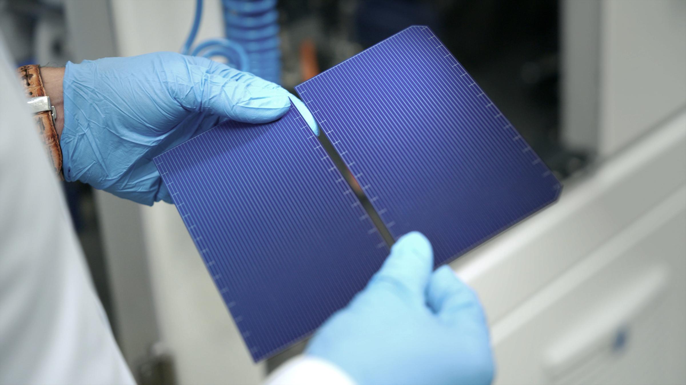 "WISO-Dokumentation: Die fetten Jahre sind vorbei - Was die Wirtschaft jetzt braucht": Zwei Hände in blauen Einweghandschuhen halten zwei kleine, blaue Solarmodule.