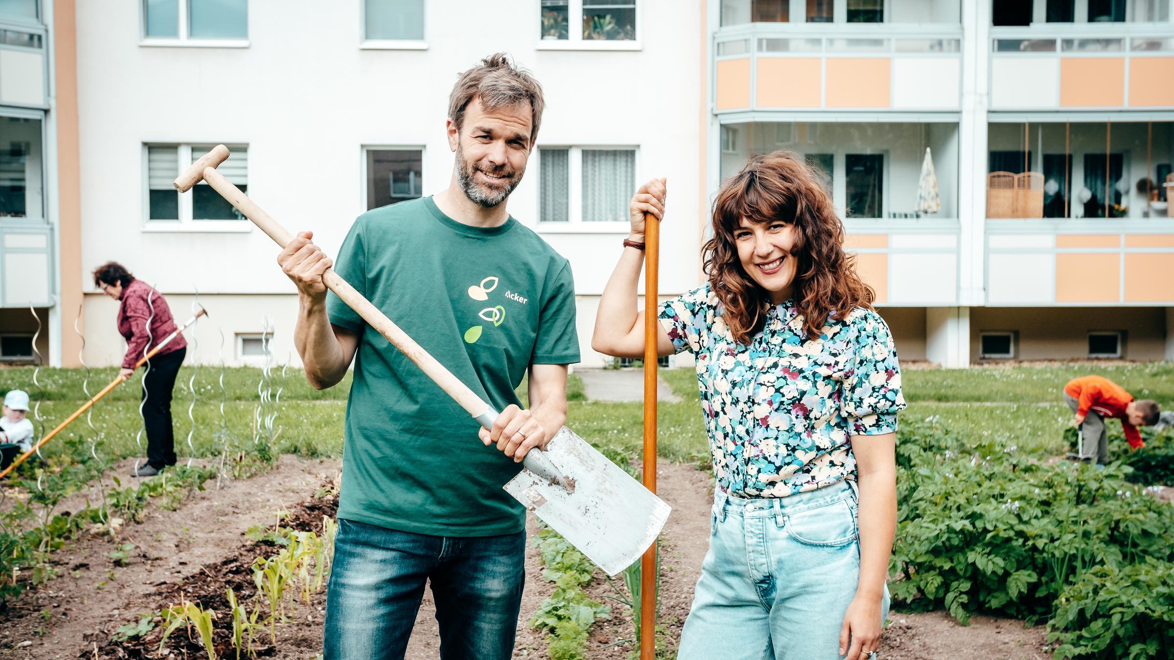 "plan b: Da geht was, Deutschland! - Wer arbeitet für eine saubere Zukunft?": Christoph Schmitz und Reporterin Antonia Lily Schanze stehen in einem Gemüsegarten vor einer Hochhaussiedlung.