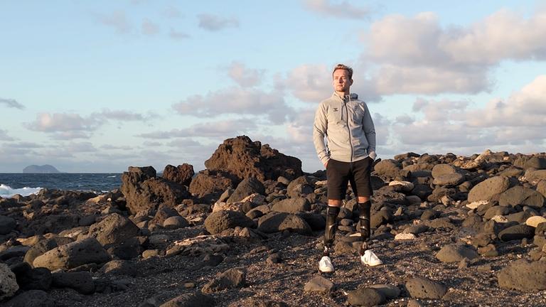 "sportstudio reportage: Paralympische Helden - Meister ihres Schicksals": Para Leichtathlet Johannes Floors im Trainingslager unmittelbar vor den Paralympics: Er steht an einer felsigen Küste und blickt zur Seite, im Hintergrund liegt das Meer.