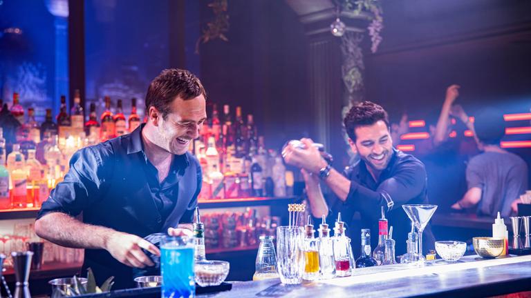 "Nightlife": Milo (Elyas M'Barek) und Renzo (Frederick Lau) stehen in der Bar hinter dem Tresen und mixen lachend Cocktails.