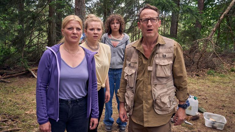 "Blackout bei Wellmanns": Thomas Wellmann (Wotan Wilke Möhring), Eva (Jördis Triebel), Paula (Daria Vivien Wolf) und Jenny (Josefine Keller) stehen auf einer Waldlichtung. Thomas trägt Funktionskleidung, die restlichen Familienmitglieder einfache Klamotten. Die Familie blickt mit erstaunten Gesichtern nach vorne.