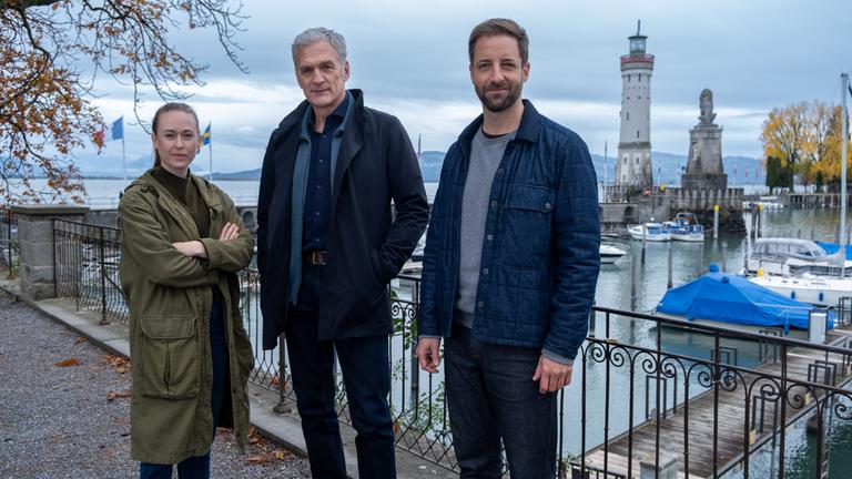 "Der Kommissar und der See - In besseren Kreisen": Annika Wagner, Robert Anders und Martin Keller stehen im Hafen einer Stadt und blicken in die Kamera.