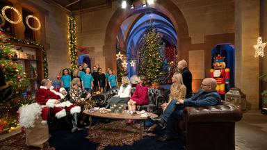 "Der 'Bares für Rares'-Weihnachtsabend - mit Horst Lichter und Freunden": Walter Lehnertz, Fabian Kahl, Dr. Bianca Berding, Wendela Horz, Horst Lichter, Dr. Elisabeth Nüdling und Sven Deutschmanek sitzen auf Sofas und schauen erwartungsvoll nach hinten, wo ein Kinderchor auftritt. Der Raum ist mit Weihnachtsdekoration geschmückt.