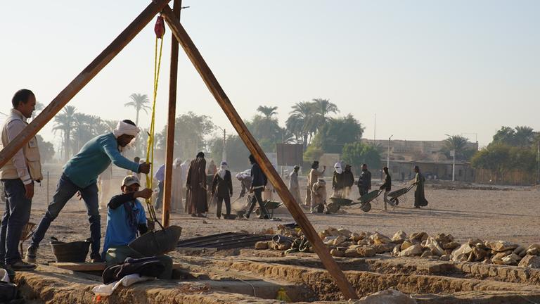 "Terra X: Ägyptens vergessene Gräber": Auf der Ausgrabungsstätte: Arbeiter leeren mit Hilfe eines einfachen Flaschenzuges einen Schacht. Im Hintergrund sind weitere Arbeiter, einige fahren Schubkarren.