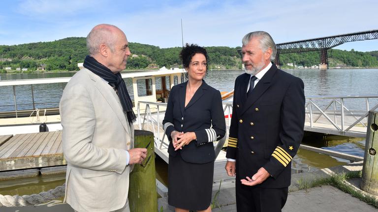 "Das Traumschiff: Hudson Valley": Vor einem Bootsanleger: Mit erklärender Gestik steht Staff-Kapitän Martin Grimm (Daniel Morgenroth) vor Hendrik Hansen (Peter Kremer). Hanna Liebhold (Barbara Wussow) steht neben ihm und blickt Martin unterstützend an.
