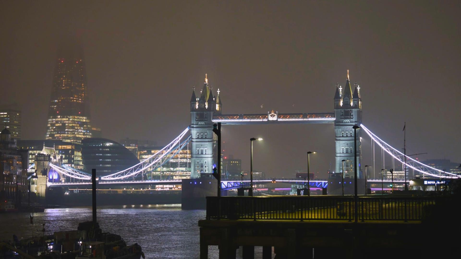 Blick auf London bei Nacht mit der beleuchteten Tower Bridge und mit Nebel im Hintergrund.