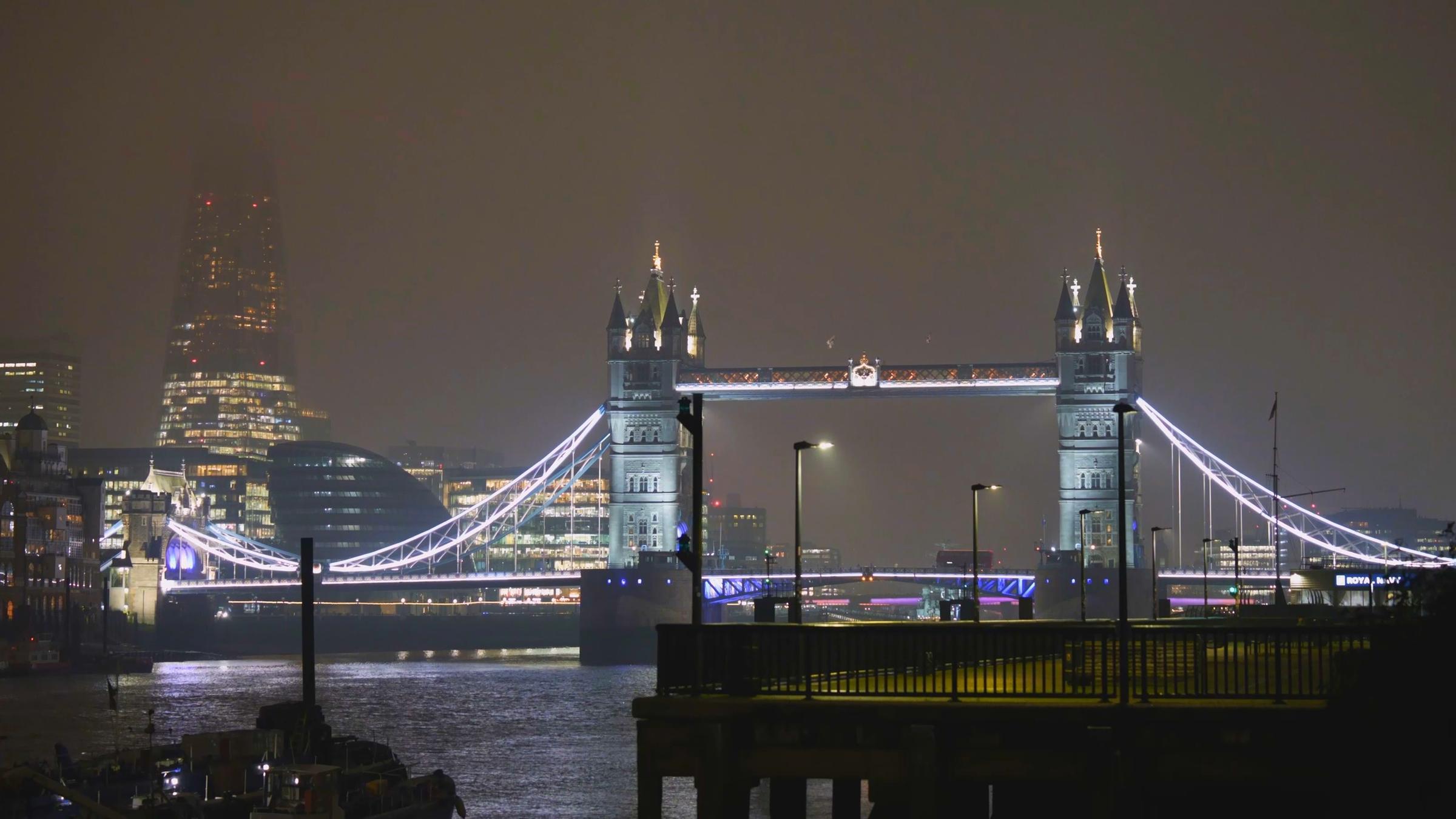 Blick auf London bei Nacht mit der beleuchteten Tower Bridge und mit Nebel im Hintergrund.
