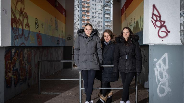 "37 Grad: Vererbte Armut - Kindheit mit wenig Geld": Angie (18), Luisa (16) und ihre Mutter Silvana (36) stehen an Stangen gelehnt in einem Hausdurchgang. In dem Gang befinden sich Graffitis, dahinter steht ein Hochhaus.