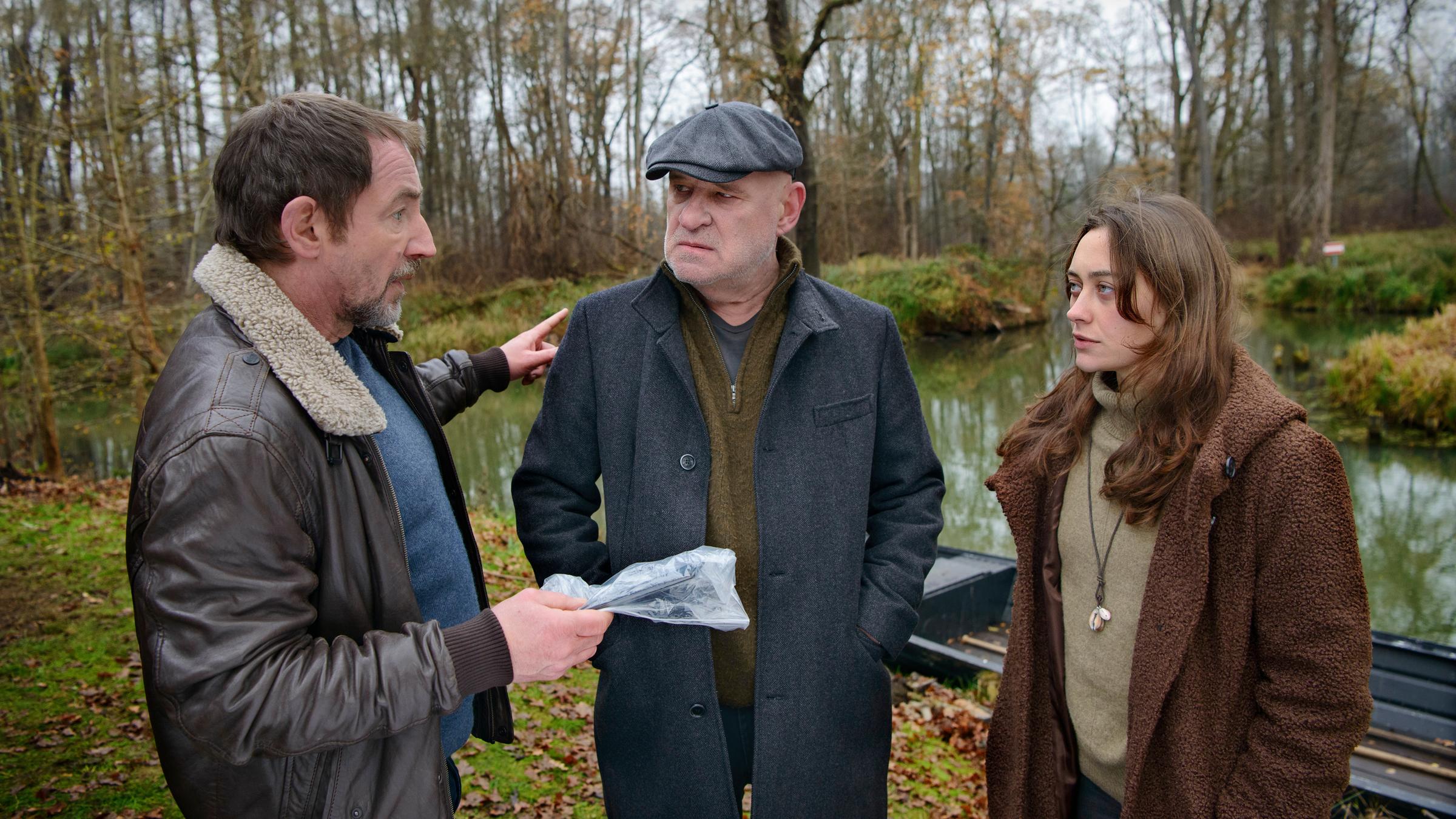"Spreewaldkrimi - Bis der Tod euch scheidet": Kriminalrat a.D. Krüger (Christian Redl) und Hauptkommissar Fichte (Thorsten Merten) stehen zusammen mit Fina Jurisch (Mercedes Müller) draußen vor einem Kahn und besprechen sich.